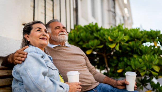 Hispani senior couple sitting outside on a bench and drinking coffee