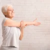 A senior female doing a shoulder stretch indoors.