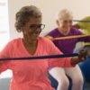 A group of seniors (three) sitting on gymnastic balls with resistant bands.