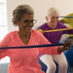 A group of seniors (three) sitting on gymnastic balls with resistant bands.
