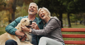 A happy senior couple sitting outside on a bench with their dog.