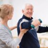 A senior male lifting dumbbells with a female personal trainer.