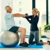 Senior on exercise ball doing fitness with personal adult female trainer.
