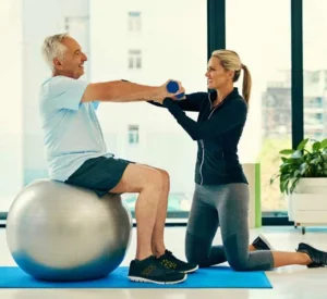 Senior on exercise ball doing fitness with personal adult female trainer.