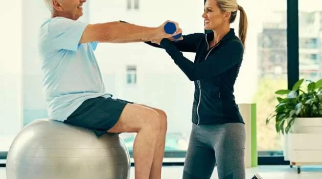 Senior on exercise ball doing fitness with personal adult female trainer.