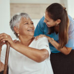 A female caregiver smiling at a female senior in her home.