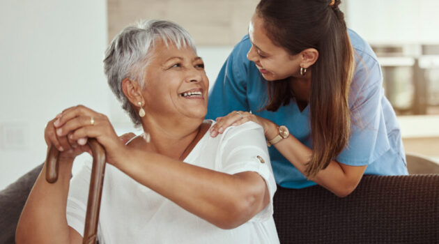 A female caregiver smiling at a female senior in her home.