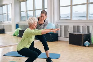 A female senior doing a fall prevention exercise with a younger female adult trainer.