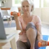 A senior woman is exercising in front of a computer, following a virtual fitness class.